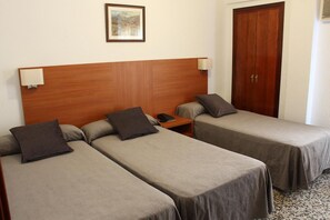 A hotel room with two single beds, a wooden headboard, bedside lamps, a nightstand, a telephone, and a wooden door. - Hotel Jardin (Oropesa del Mar)