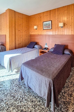 Habitación de hotel con dos camas, paneles de madera en la pared, un cuadro enmarcado y una mesita de noche con una lámpara.