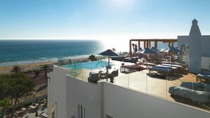 A rooftop pool area with lounge chairs and umbrellas, overlooking a beach and the sea. - Daia Slow Beach Hotel Conil - Adults Only (Conil de la Frontera)