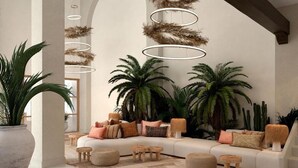 A modern living room with a sectional sofa, multiple poufs, and a large potted plant. - Daia Slow Beach Hotel Conil - Adults Only (Conil de la Frontera)