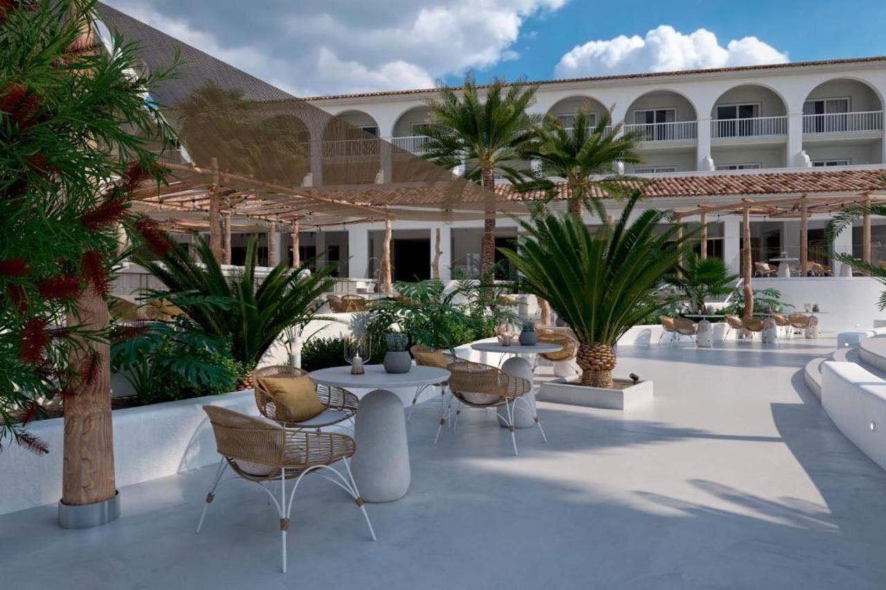 A spacious outdoor area with multiple seating arrangements, palm trees, and a building with arched windows in the background.