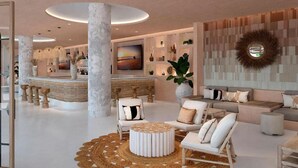 A modern lobby with a central reception desk, seating area, and a large wall-mounted TV. - Daia Slow Beach Hotel Conil - Adults Only (Conil de la Frontera)