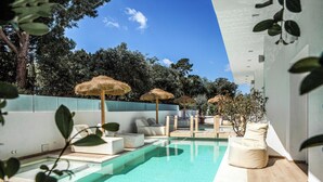 Ein moderner Poolbereich mit klarem Wasser, Liegestühlen und strohgedeckten Sonnenschirmen.