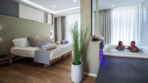 Ein modernes Hotelzimmer mit Bett, einer Sitzecke, einer großen Topfpflanze und einem separaten Badezimmer mit Badewanne.