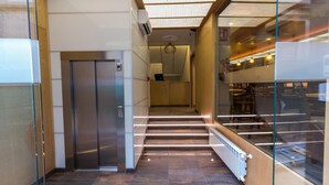 A modern elevator with a metallic finish, a glass wall on one side, and a tiled floor. - Hotel Novo Candido (Ourense)