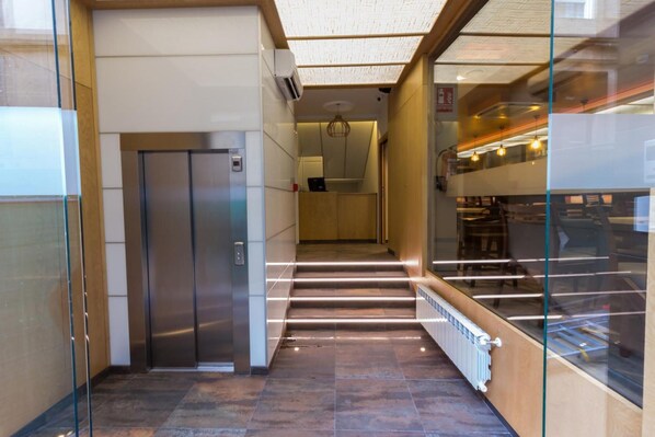 En moderne elevator med metalfinish, en glasvæg på den ene side og et flisebelagt gulv.