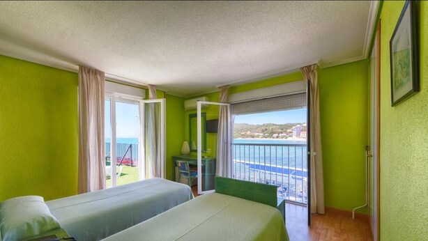 A room with two beds, a small table, and a view of the sea. - Hotel Marina (Oropesa del Mar)