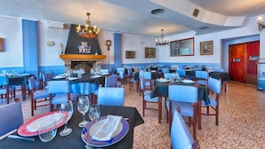 A restaurant with multiple tables, chairs, and a central fireplace. - Hotel Marina (Oropesa del Mar)