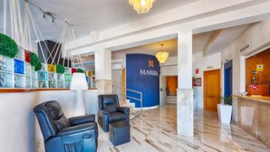 A lobby with a reception desk, black leather chairs, a blue wall with the word 'MARINA,' and a marble floor. - Hotel Marina (Oropesa del Mar)