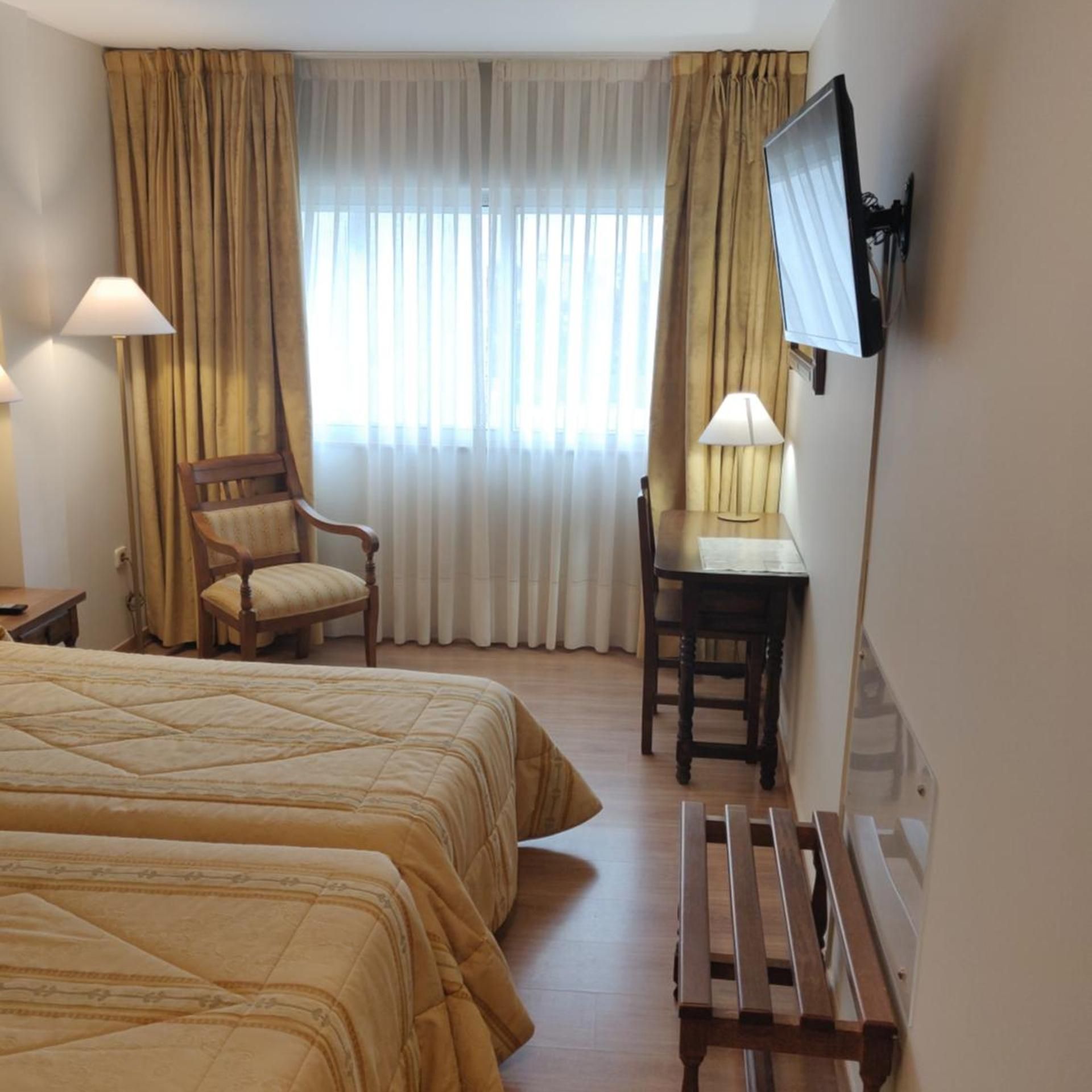 Una habitación de hotel con cama, escritorio, silla y televisión montada en la pared.