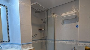 Un baño moderno con ducha de vidrio, un lavamanos blanco con espejo y un inodoro.