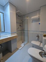 Un baño moderno con ducha de vidrio, un lavamanos blanco con espejo y un inodoro.