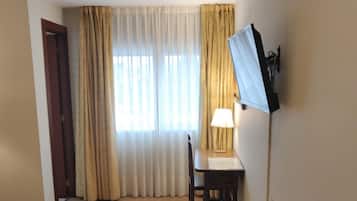 Habitación de hotel con cama, escritorio, silla, televisor montado en la pared y ventana con cortinas.