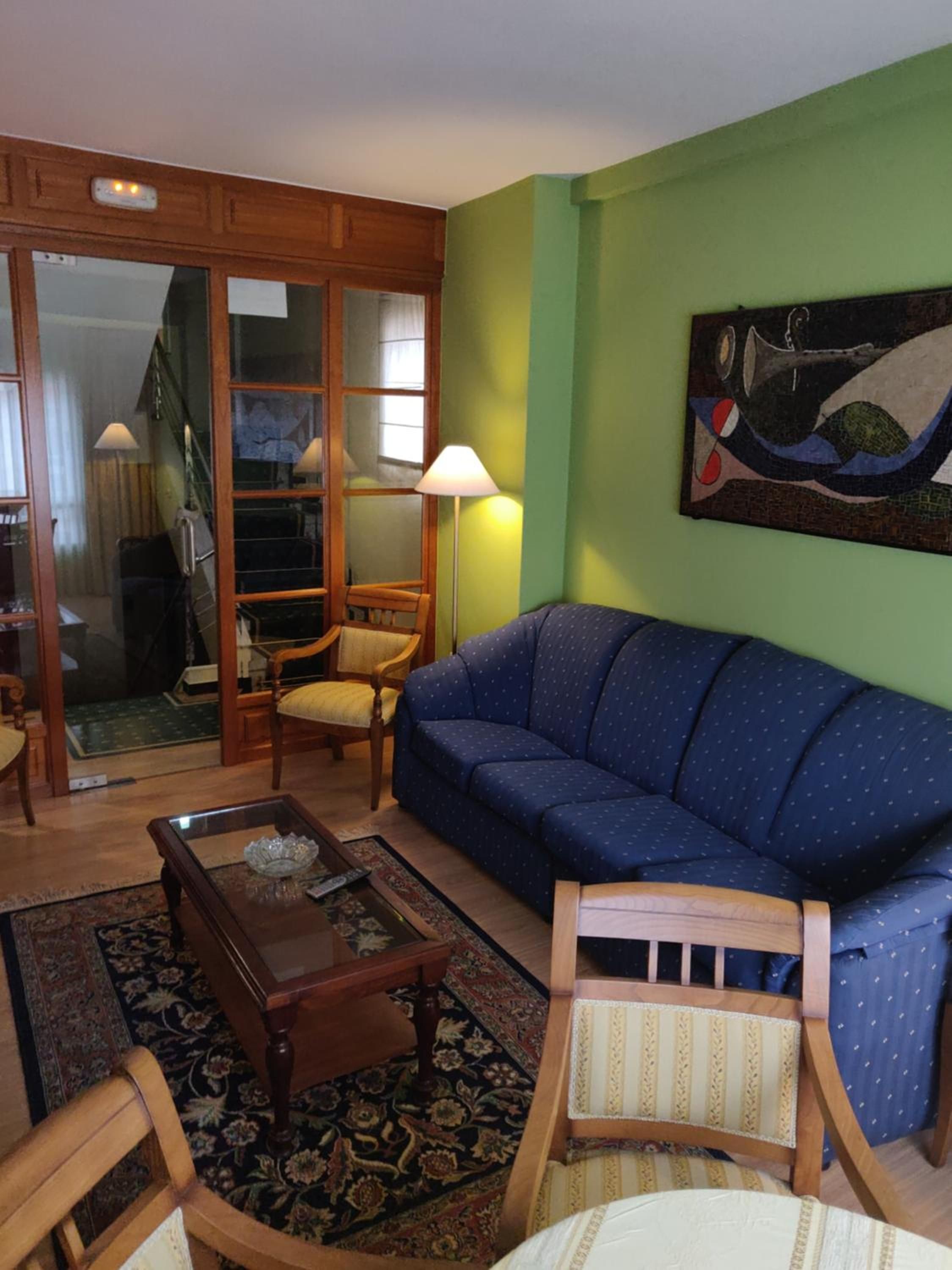 Una sala de estar con un sofá azul, sillas de madera, una mesa de centro y un cuadro en la pared.
