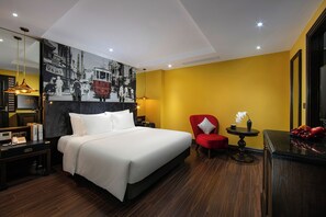 A hotel room with a large bed, a red armchair, a small table with a vase, and a wall-mounted artwork depicting a vintage tram. - Ha Noi Lion Boutique Hotel (Hanoi)