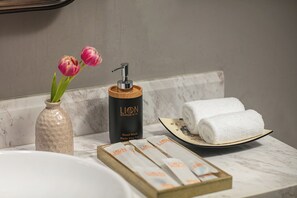 Un meuble-lavabo de salle de bain avec un plan de toilette en marbre, un distributeur de savon liquide, un vase avec des fleurs et un plateau avec des serviettes.