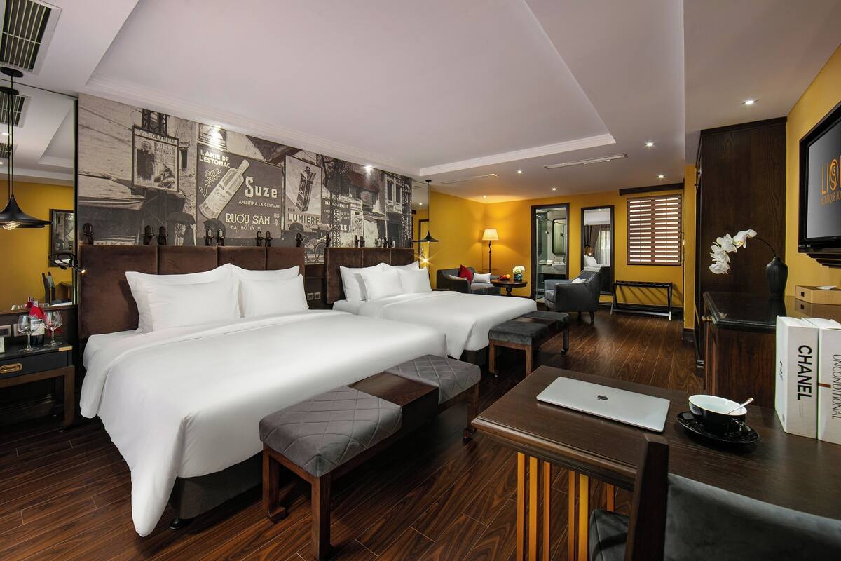 Habitación de hotel con dos camas, un escritorio, una computadora portátil, una caja de Chanel y un espejo.