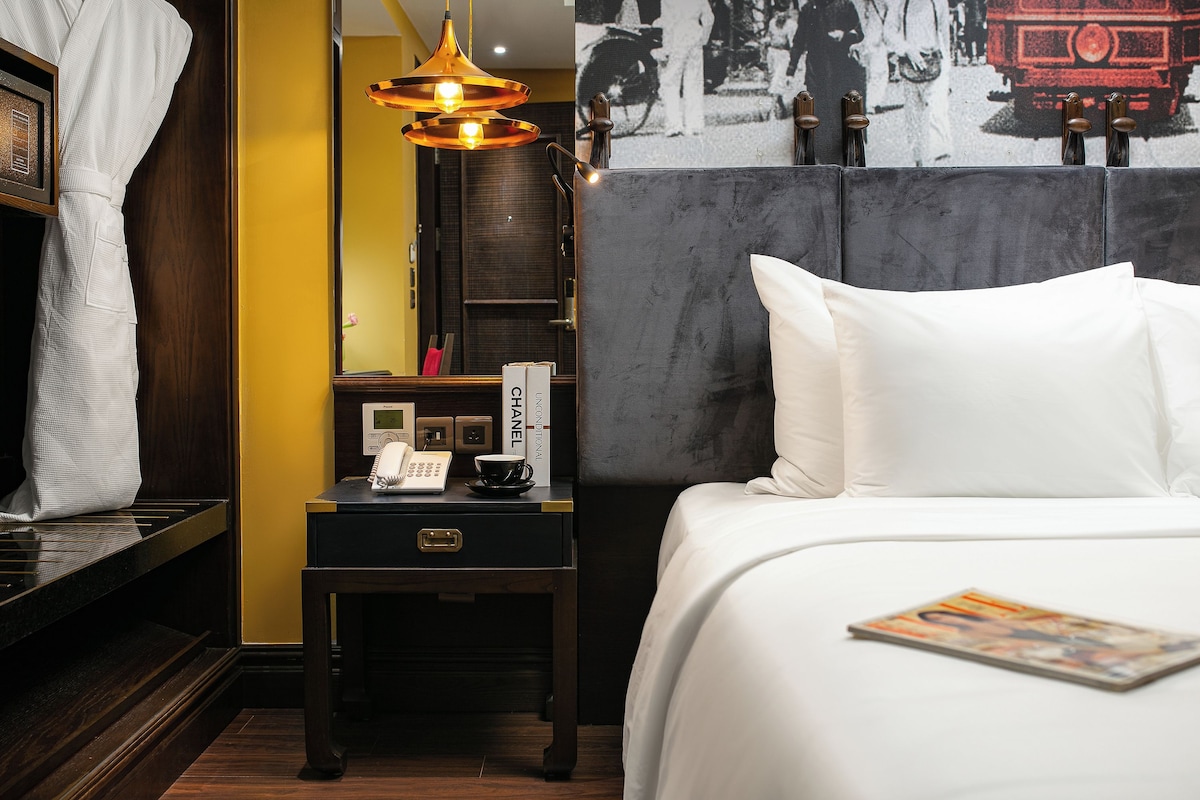 Ein Hotelzimmer mit einem Bett, einem Nachttisch mit Telefon, einer Lampe und einer Zeitschrift auf dem Bett.