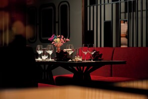 Un restaurant à la lumière tamisée, avec une table dressée pour deux personnes, agrémentée d’un vase de fleurs et de verres à vin.