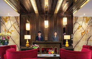 Een hotel receptie met marmeren wanden, rode stoelen en een receptiebalie.