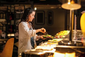 Uma pessoa servindo comida em um buffet, com diversos pratos à mostra.