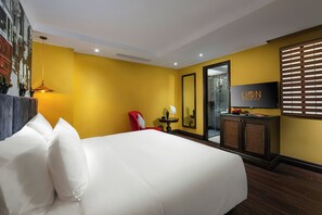 Une chambre d’hôtel avec un grand lit, un fauteuil rouge, une petite table avec un vase, un miroir et un téléviseur fixé au mur.