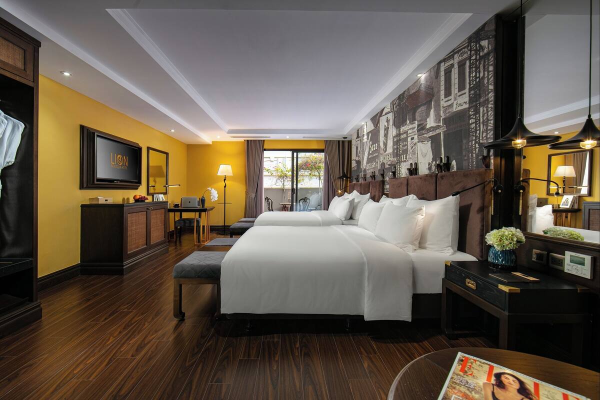 Habitación de hotel con una cama grande, un escritorio, una silla, un armario, un televisor y un ventanal amplio.