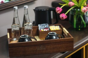 Un plateau en bois avec trois bouteilles en verre, une théière noire et une boîte de chocolats.