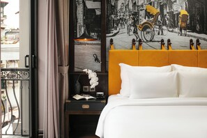 Et hotelværelse med en seng, et natbord med lampe, et billede i ramme og udsigt til gaden.
