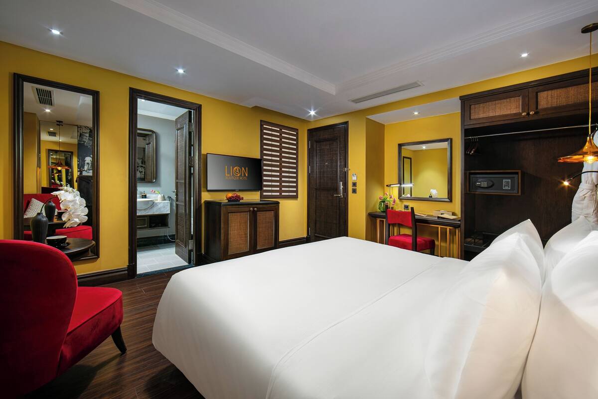 Una habitación de hotel con una cama grande, un sillón rojo, un escritorio con una silla, un televisor y un armario.