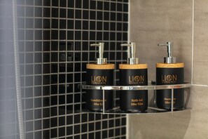 Trois distributeurs noirs, dotés d’une base en bois et portant l’inscription « LION Boutique Hotel », sont placés sur une étagère en métal.