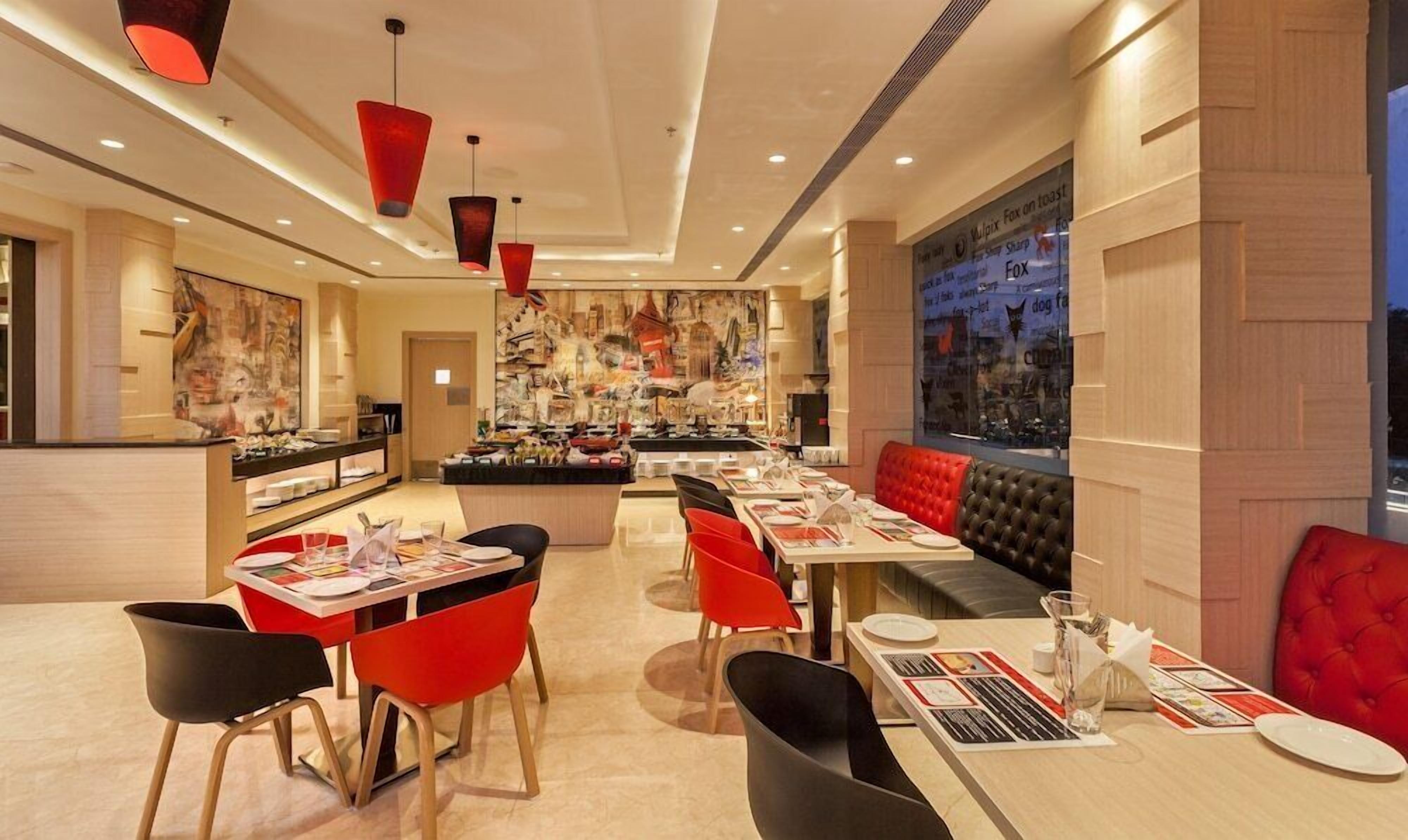A modern restaurant interior with red and black chairs, a central bar area, and a large window with a city view.