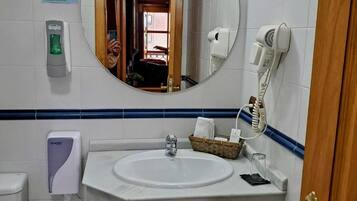 Un baño con un lavamanos blanco, un espejo, un secador de pelo, un secador de manos y un cubo de basura.