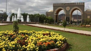 A landscaped area with a fountain, a large archway, and a flower bed. - Waqf Othman Bin Affan Hotel (Madinah)