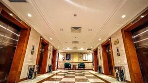 A hotel lobby with a checkered floor, two green chairs, and two elevators. - Waqf Othman Bin Affan Hotel (Madinah)