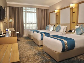 Een hotelkamer met twee bedden, een bureau, een televisie en een groot raam met gordijnen.