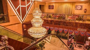A multi-level hotel lobby with a grand chandelier, a glass railing, and a seating area with patterned curtains. - Waqf Othman Bin Affan Hotel (Madinah)