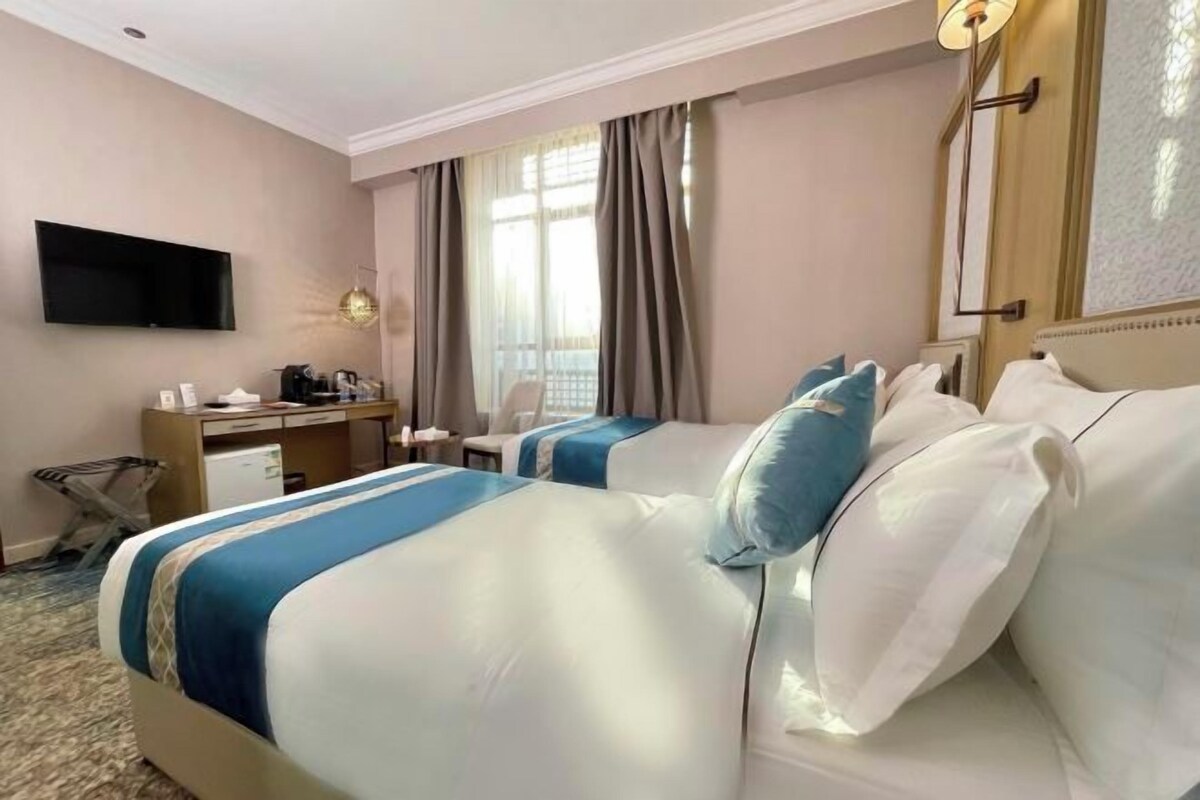 Een hotelkamer met twee bedden, een bureau, een televisie en een raam met gordijnen.