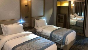 A hotel room with two beds, a large mirror, and a wardrobe. - Waqf Othman Bin Affan Hotel (Madinah)