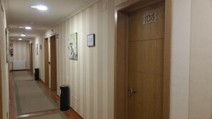 Un couloir d’hôtel avec des murs à rayures, un radiateur, une poubelle et une porte portant l’inscription « 103 ».