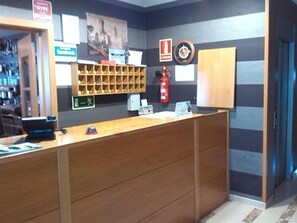 A reception desk with a computer, a fire extinguisher, and a clock on the wall. - Hotel Reina Isabel (Medina del Campo)
