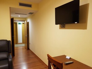 Habitación de hotel con piso de madera, televisor montado en la pared, escritorio con silla y sofá.