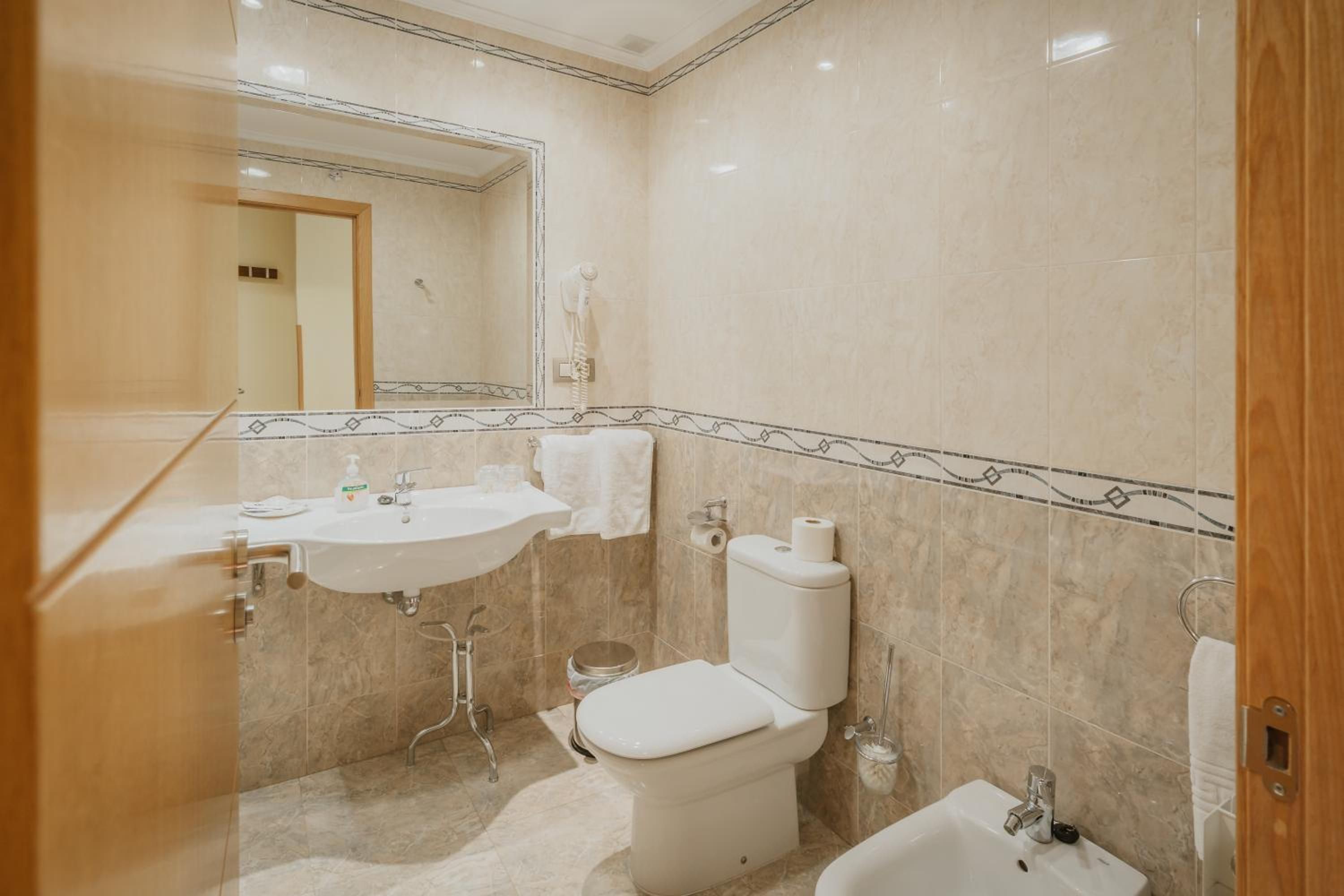 Un baño con lavamanos, inodoro, bidé y espejo.