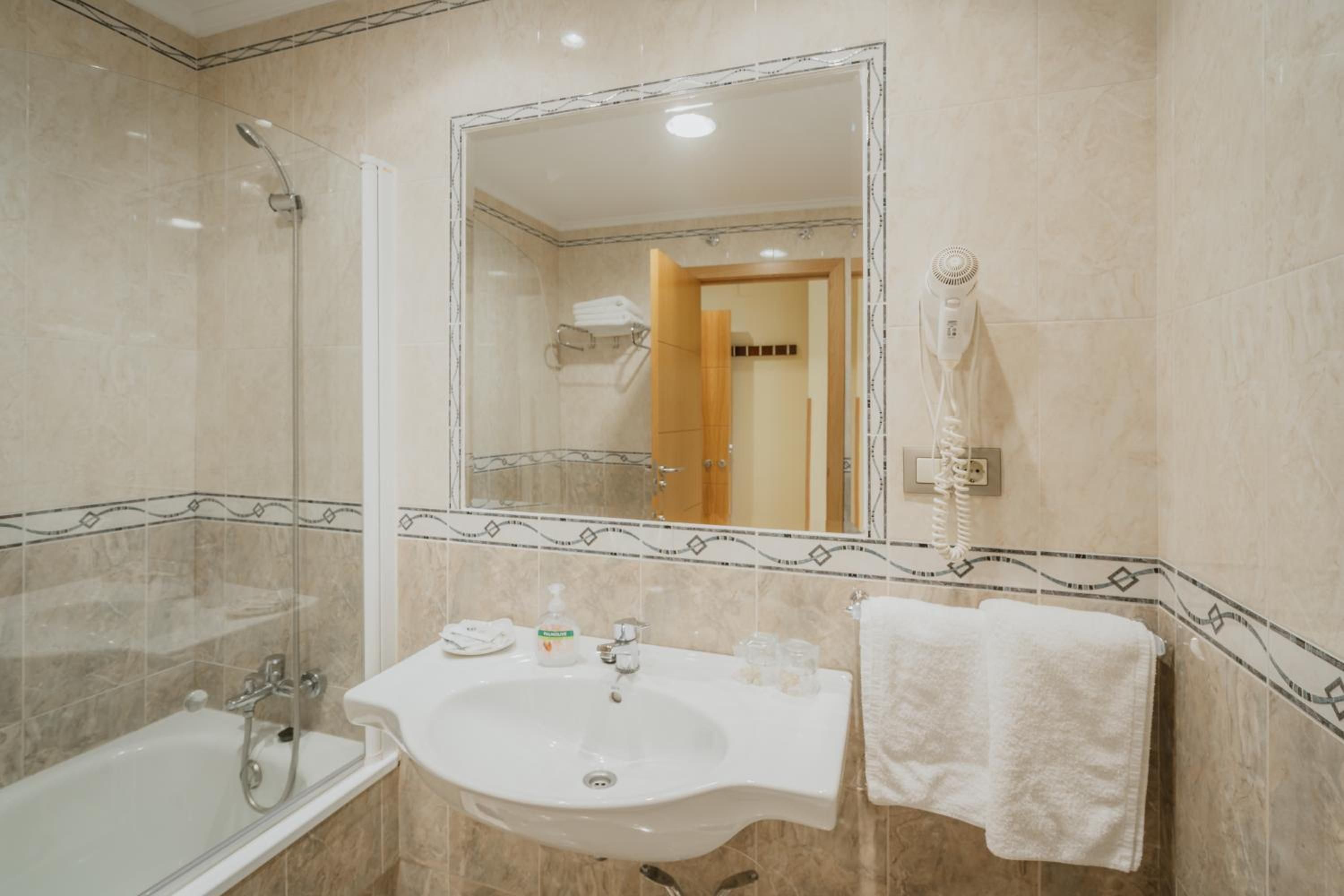 Un baño con bañera, lavamanos, espejo y secador de pelo.
