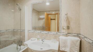 Un baño con bañera, lavamanos, espejo y secador de pelo.