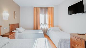 A hotel room with two beds, a desk, a TV, and a window with curtains.
