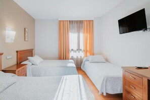 A hotel room with two beds, a desk, a TV, and a window with curtains. - Hotel Reina Isabel (Medina del Campo)