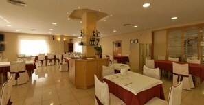 Un vaste espace dédié à la salle à manger, avec de nombreuses tables et chaises, un bar central et une grande fenêtre qui laisse entrer la lumière naturelle.