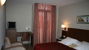 Habitación de hotel con cama, escritorio, silla, televisor y un cuadro en la pared.