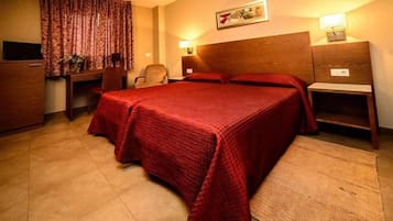 A hotel room with a large bed, a desk, a chair, a television, and a nightstand with a lamp.
